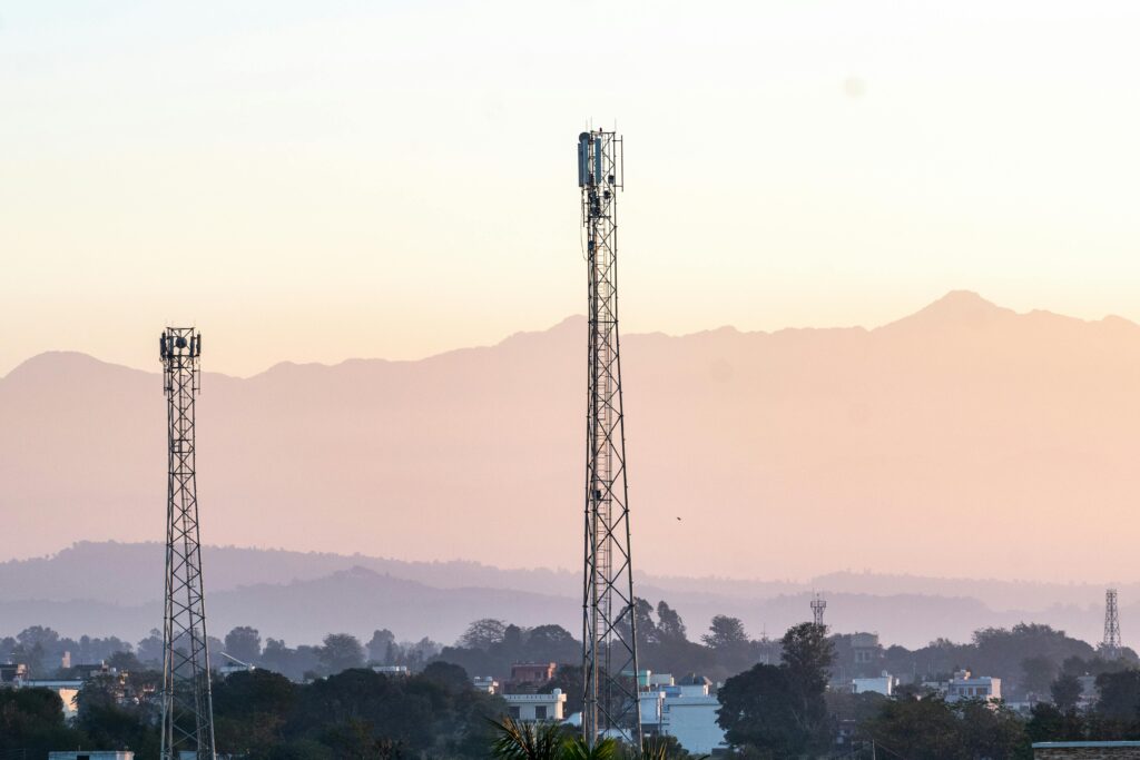 Telecom towers rise above a town against a backdrop of mountains at dawn, highlighting communication infrastructure.