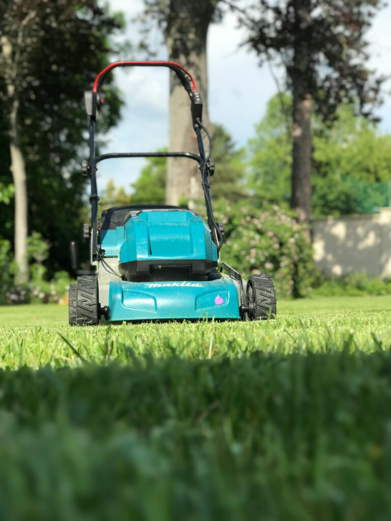 A blue lawn mower on a lush green lawn during a sunny summer day in Göd, Hungary.