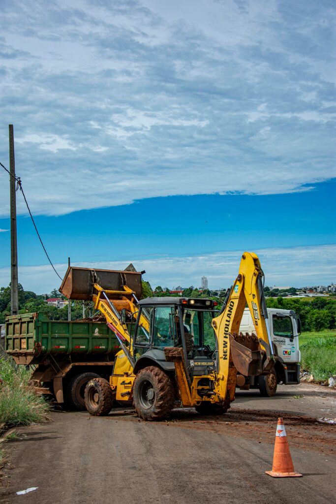 A backhoe and truck performing roadwork under a blue sky in Londrina, Brazil.