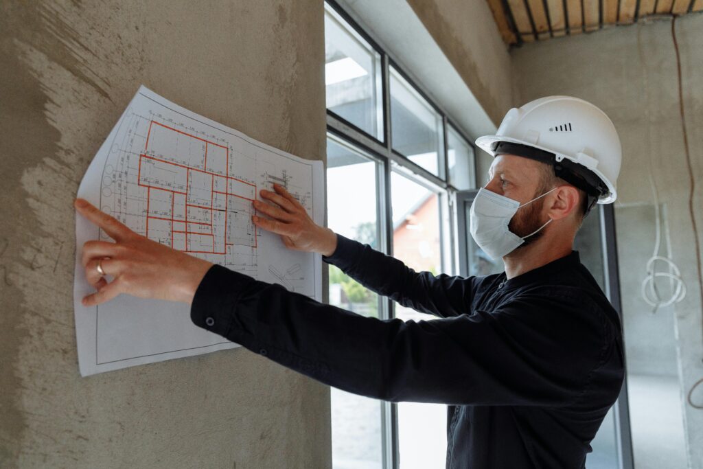 Architect wearing hard hat and mask reviews floor plans on site for new construction project.