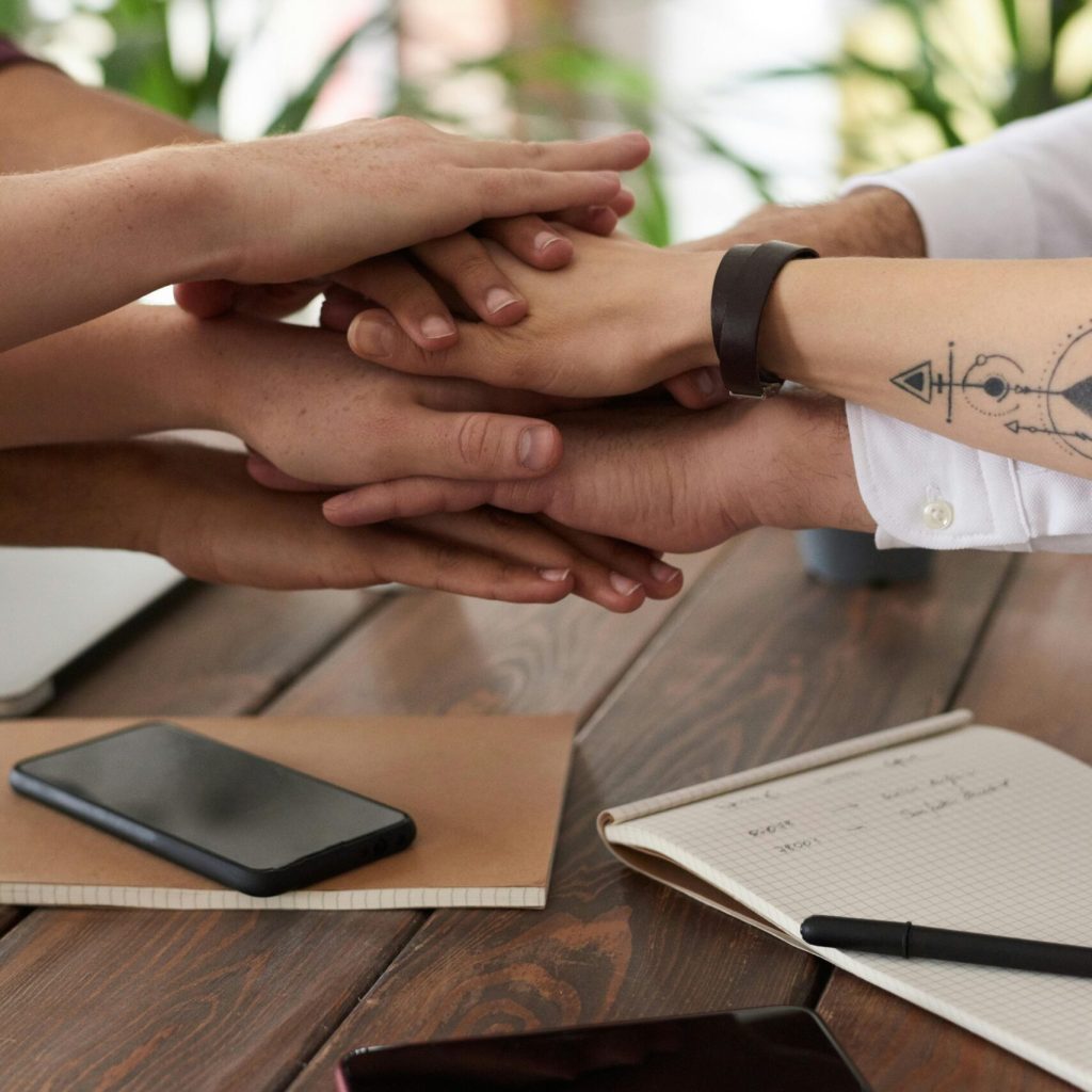 Hands from a diverse team stack on a table symbolizing unity and teamwork in a modern office setting.