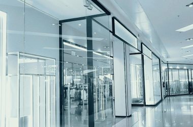 Bright and empty shopping mall corridor with glass display walls and reflections.